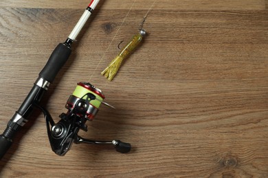 Photo of Fishing rod with spinning reel and bait on wooden background, top view. Space for text
