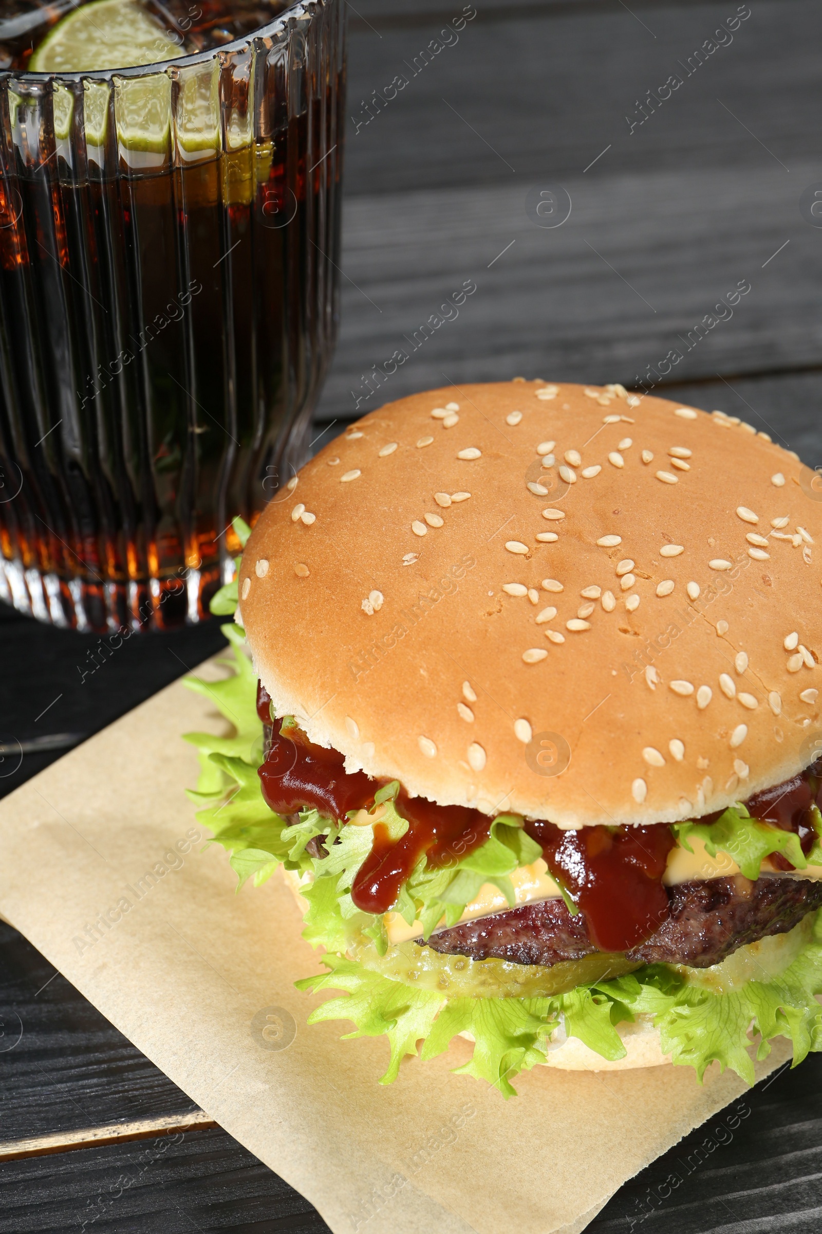 Photo of Burger with delicious patty and soda drink on black wooden table