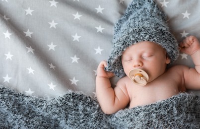 Cute newborn baby in warm hat sleeping on bed, top view