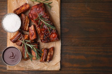 Photo of Tasty roasted pork ribs served with sauce and rosemary on wooden table, top view. Space for text