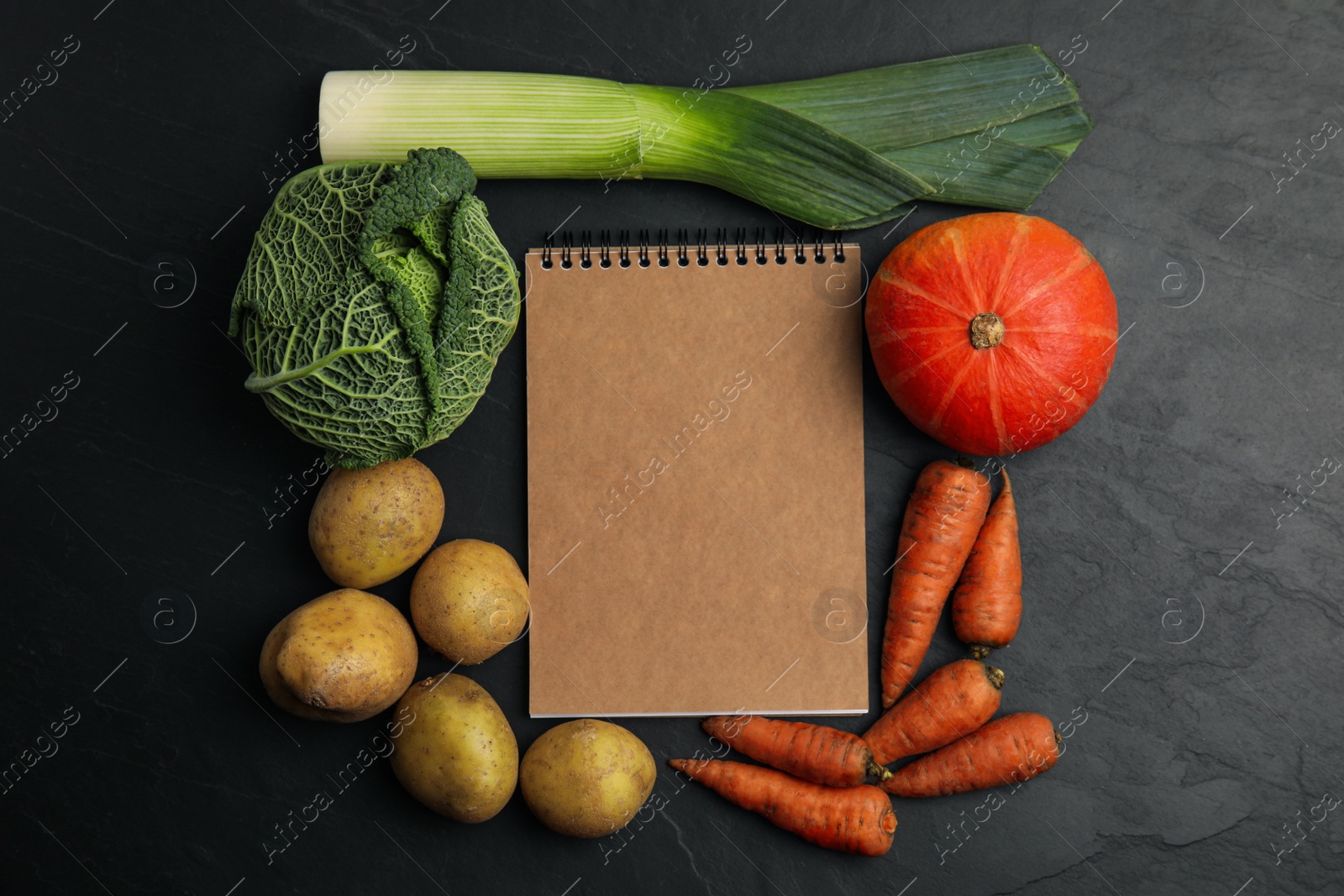 Photo of Recipe book surrounded by different fresh vegetables on black table, flat lay with space for text. Cooking classes