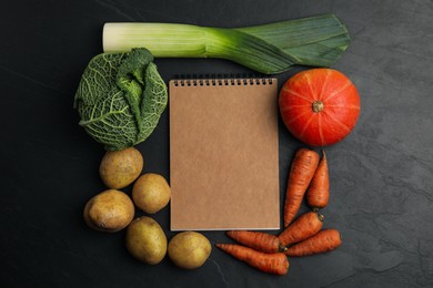 Recipe book surrounded by different fresh vegetables on black table, flat lay with space for text. Cooking classes