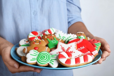 Photo of Woman with plate of delicious gingerbread Christmas cookies on grey background, closeup