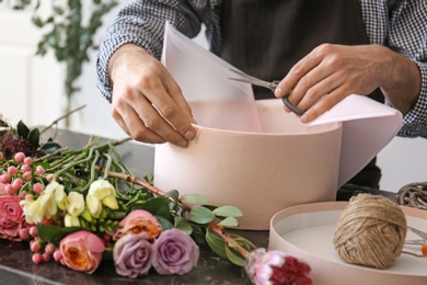 Photo of Male florist creating beautiful flower composition at table, closeup
