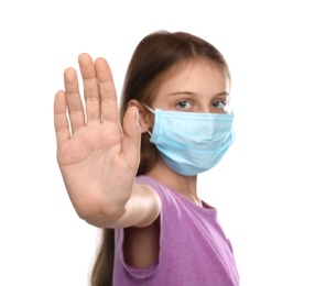 Photo of Little girl in protective mask showing stop gesture on white background. Prevent spreading of coronavirus