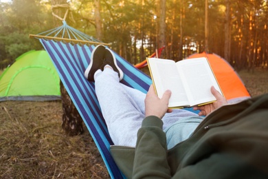 Photo of Man with book resting in comfortable hammock outdoors, closeup