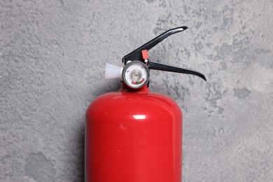 Photo of Red fire extinguisher near grey wall, closeup