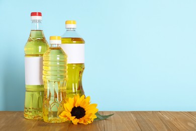 Bottles of cooking oil and sunflower on wooden table, space for text