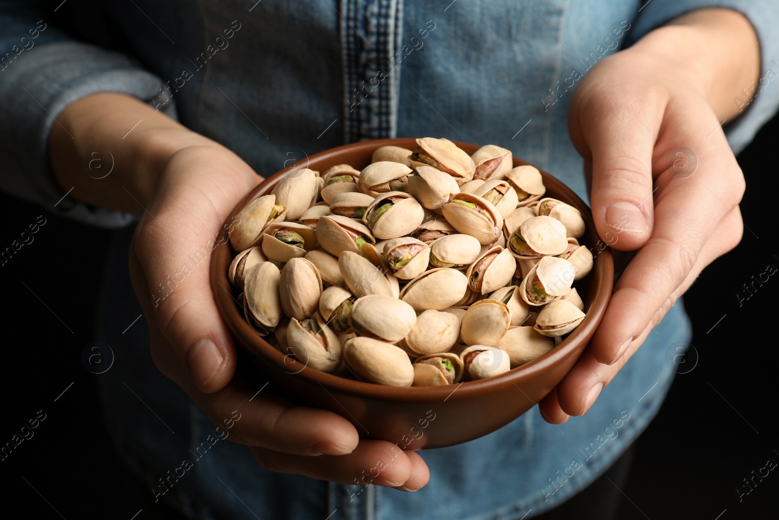 Photo of Woman holding bowl with pistachio nuts on black background, closeup