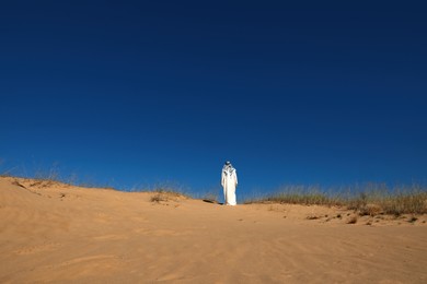 Man in arabic clothes walking through desert on sunny day, back view