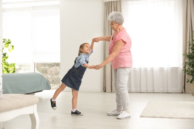 Cute girl and her grandmother dancing at home