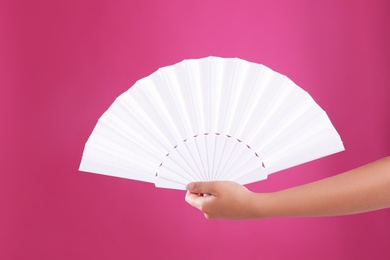 Woman holding white hand fan on pink background, closeup