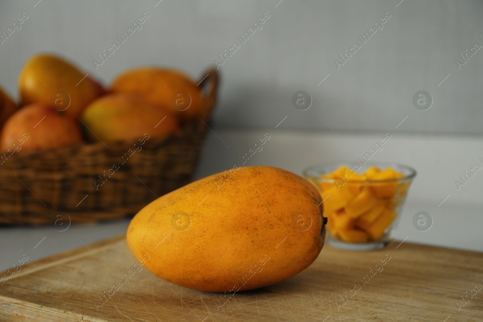 Photo of Delicious cut and whole mangoes on wooden board indoors