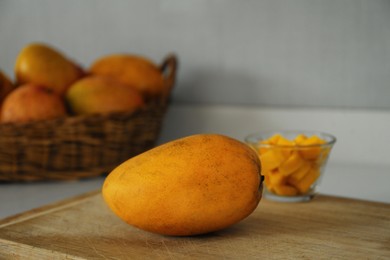 Photo of Delicious cut and whole mangoes on wooden board indoors