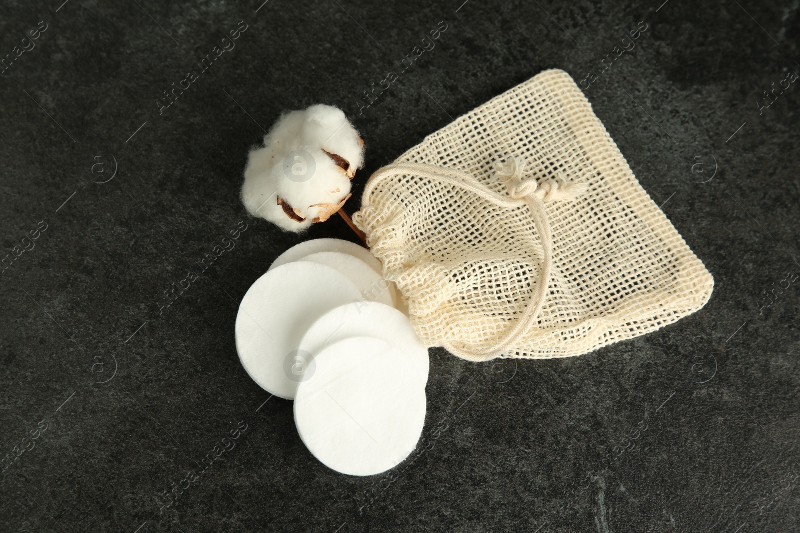 Photo of Cotton pads, bag and flower on black table, flat lay