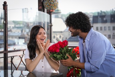 Photo of International dating. Handsome man presenting roses to his beloved woman in restaurant