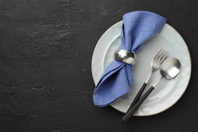 Photo of Stylish setting with cutlery, napkin and plate on dark textured table, top view. Space for text