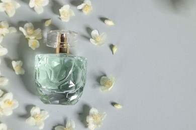 Photo of Aromatic perfume in bottle and beautiful jasmine flowers on grey background, flat lay. Space for text