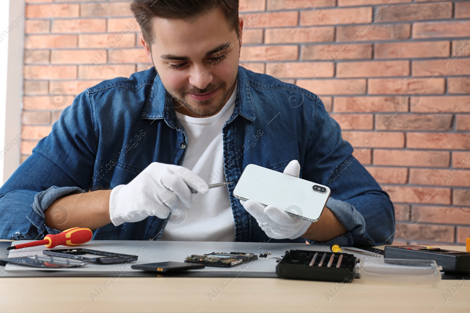 Photo of Technician repairing broken smartphone at table in workshop