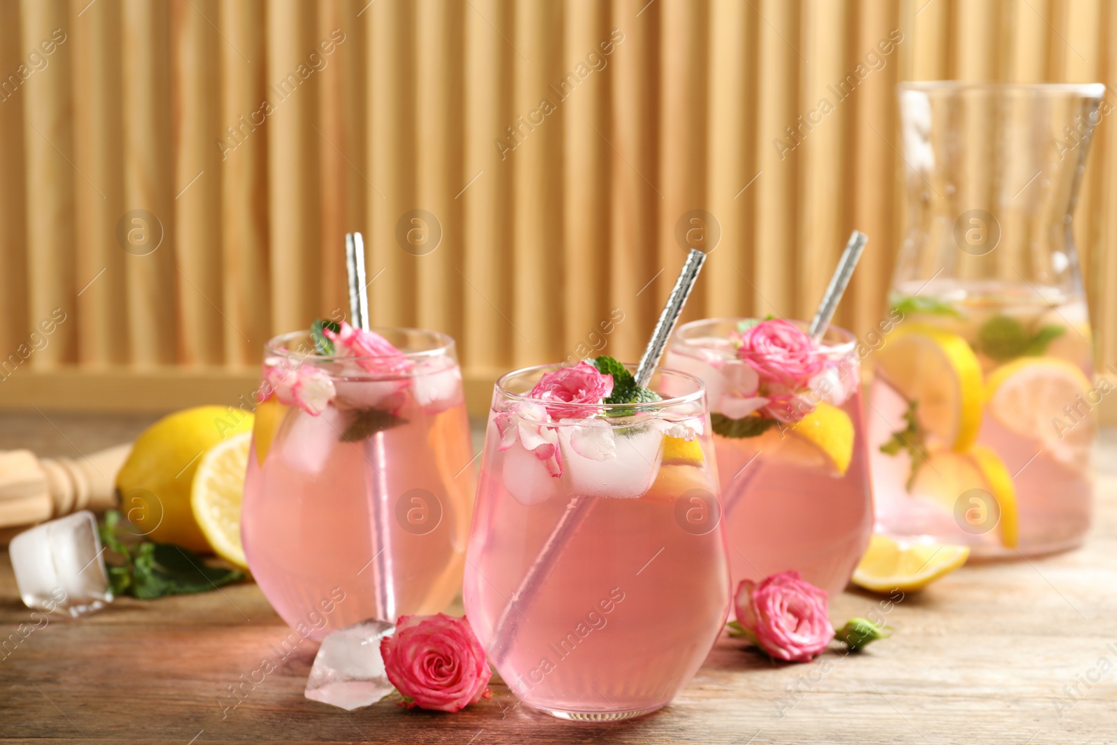 Photo of Delicious refreshing drink with rose flowers and lemon slices on wooden table