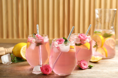 Photo of Delicious refreshing drink with rose flowers and lemon slices on wooden table
