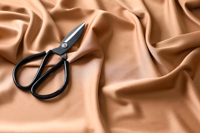 Photo of Scissors on silk fabric. Space for text