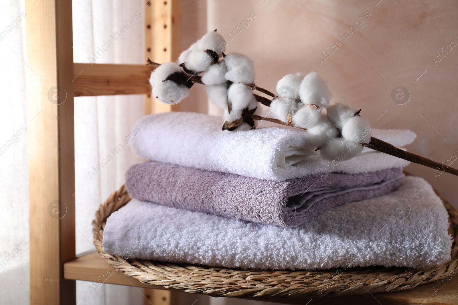 Photo of Stacked soft towels and cotton branch on wooden shelf indoors