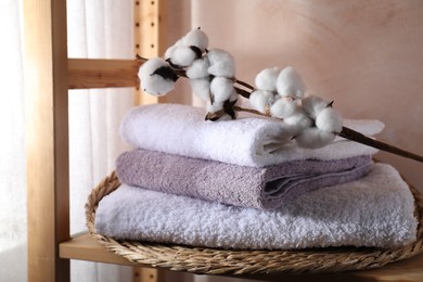 Stacked soft towels and cotton branch on wooden shelf indoors