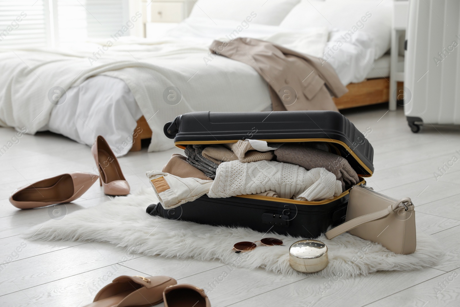 Photo of Open suitcase full of clothes, shoes and fashionable accessories on floor in bedroom