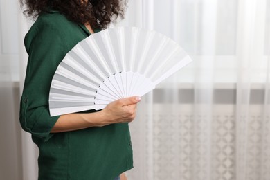 Woman with hand fan indoors, closeup. Space for text