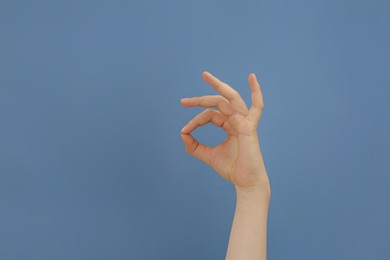 Photo of Woman showing okay gesture on pale blue background, closeup