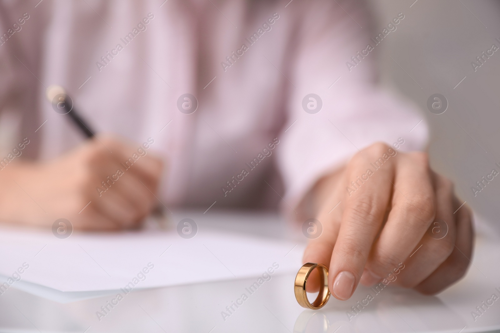 Photo of Woman with wedding ring signing divorce papers at table indoors, closeup. Space for text