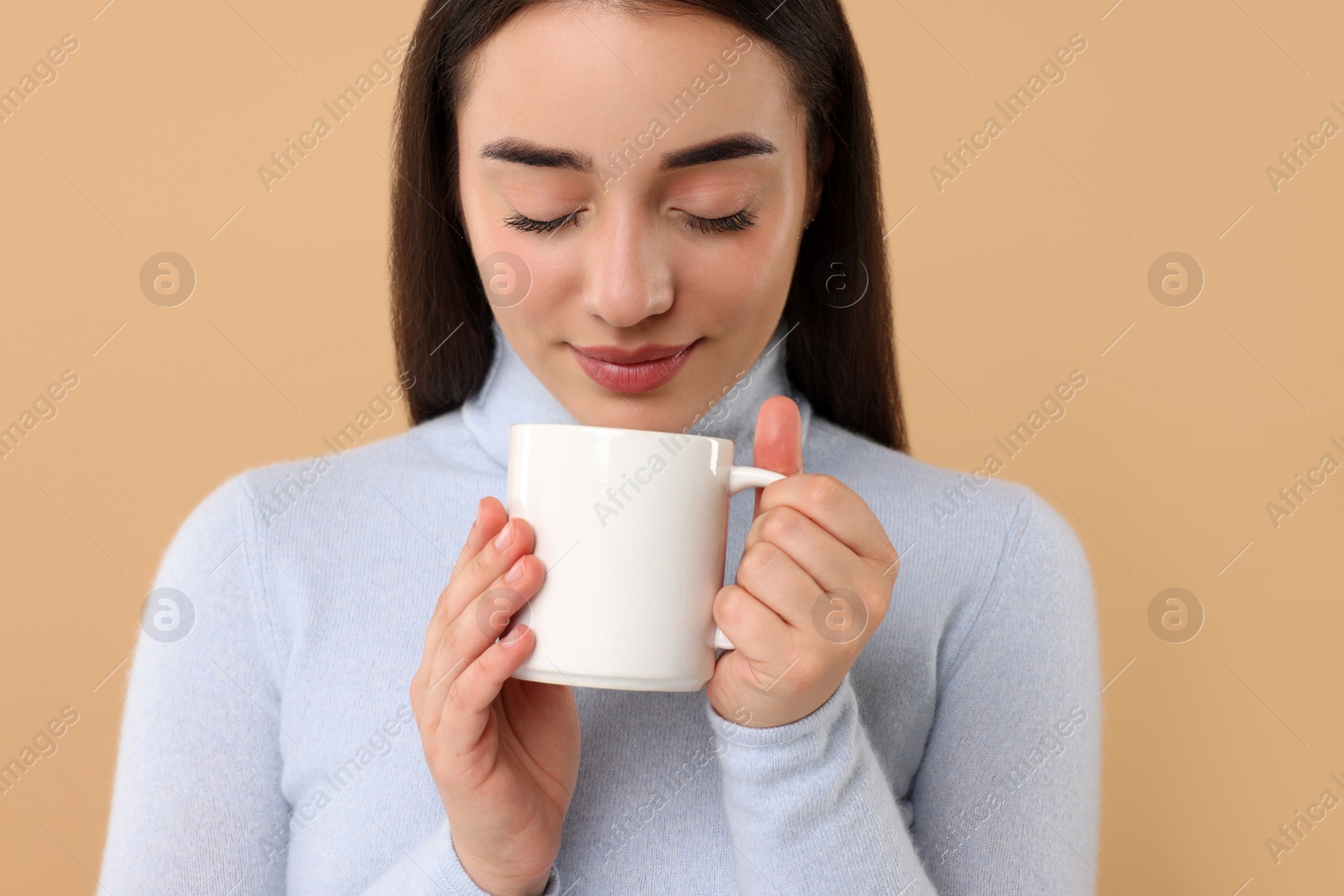 Photo of Beautiful young woman holding white ceramic mug on beige background