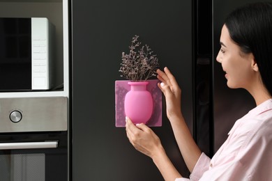 Photo of Happy woman with dried flowers and silicone vase attached to refrigerator in kitchen