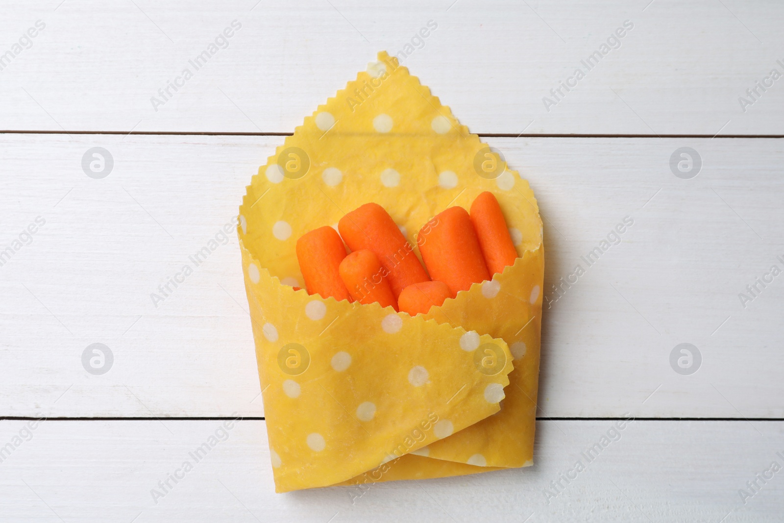 Photo of Many baby carrots in beeswax food wrap on white wooden table, top view