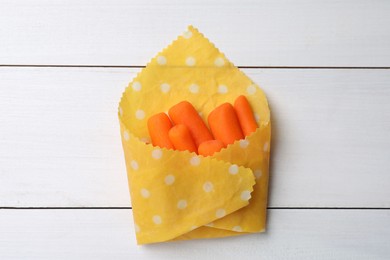 Photo of Many baby carrots in beeswax food wrap on white wooden table, top view