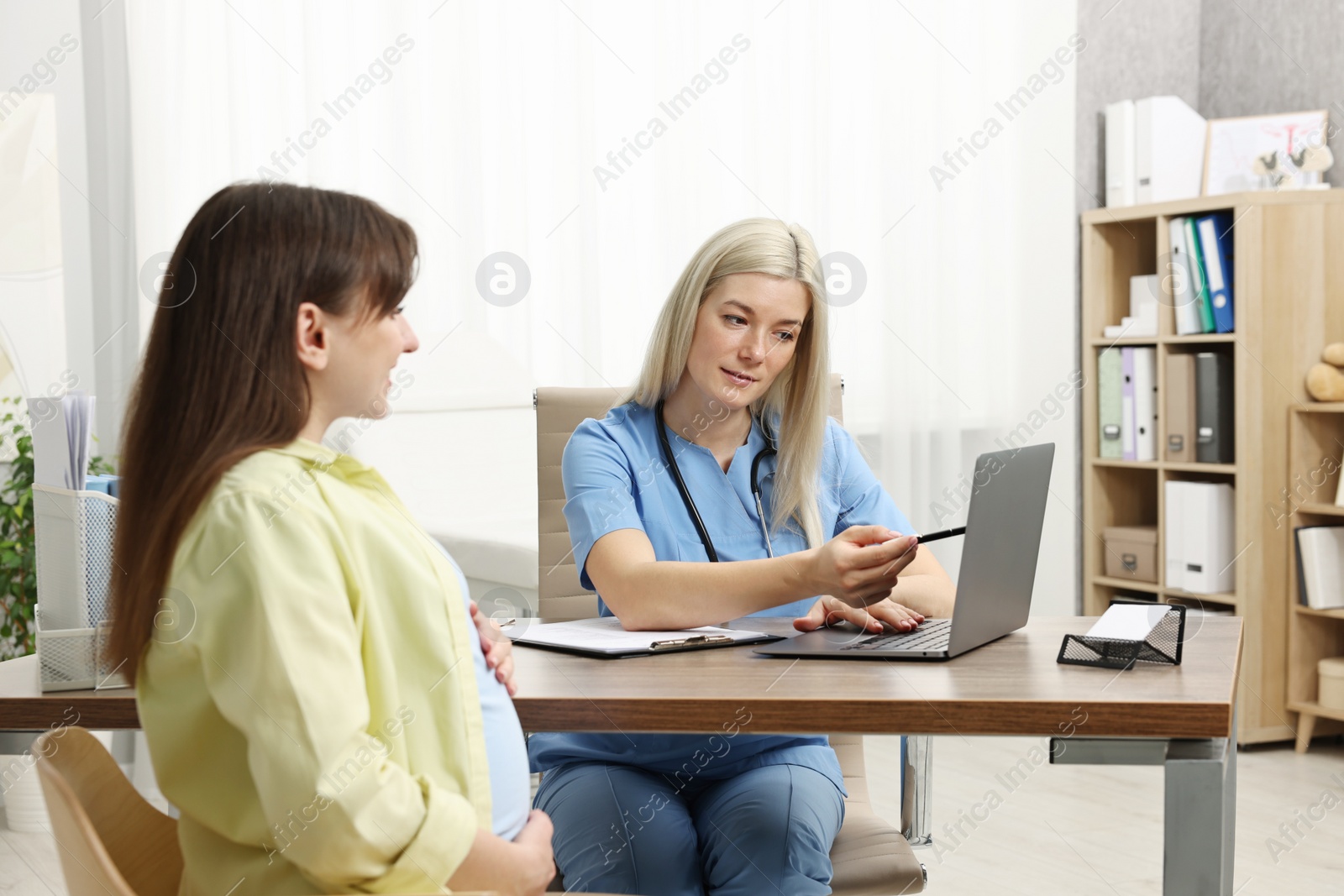 Photo of Doctor consulting pregnant patient at table in clinic