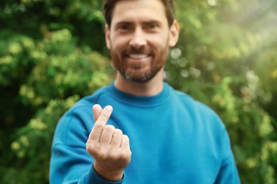 Happy man showing heart gesture outdoors, focus on hand