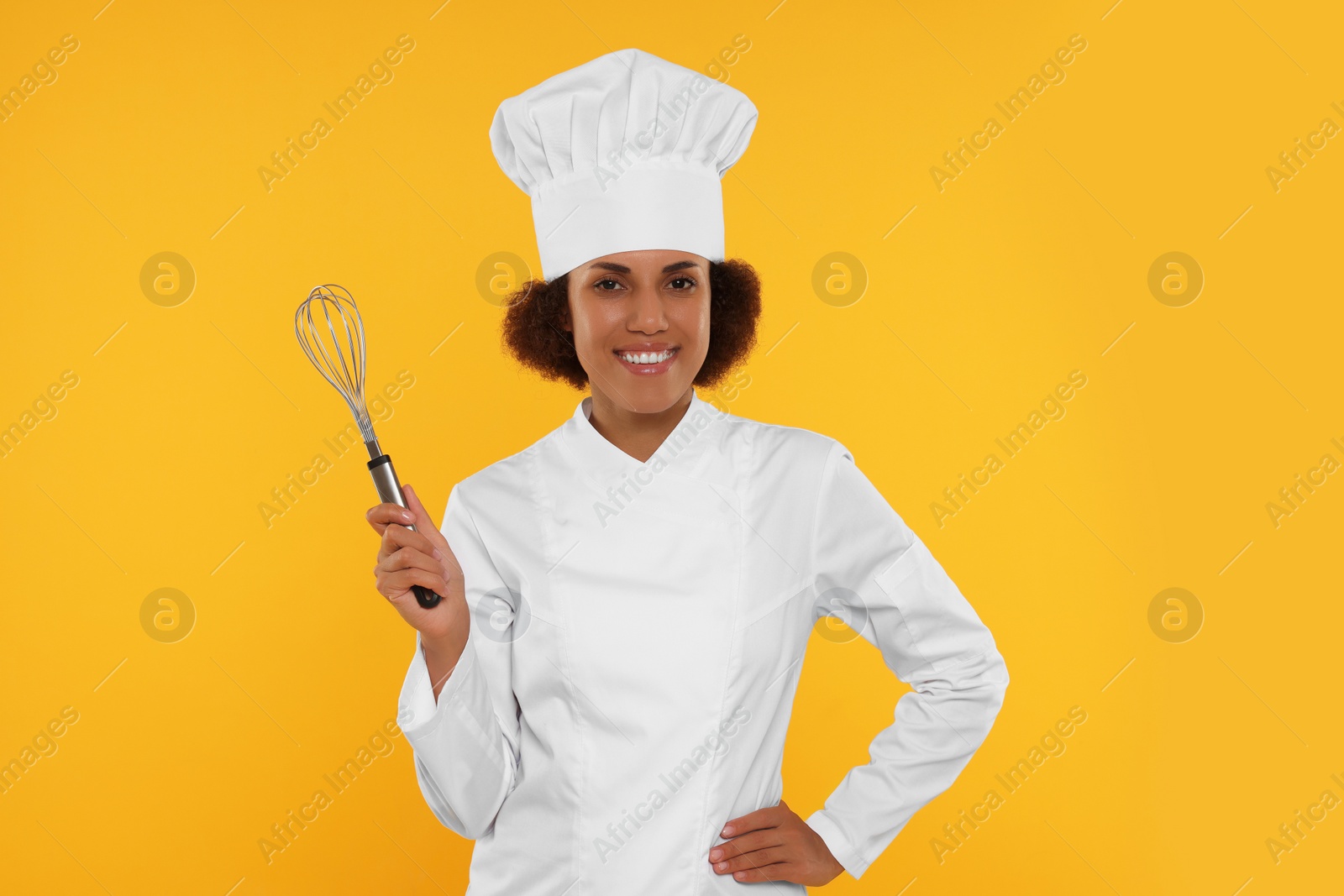 Photo of Happy female chef in uniform holding whisk on orange background