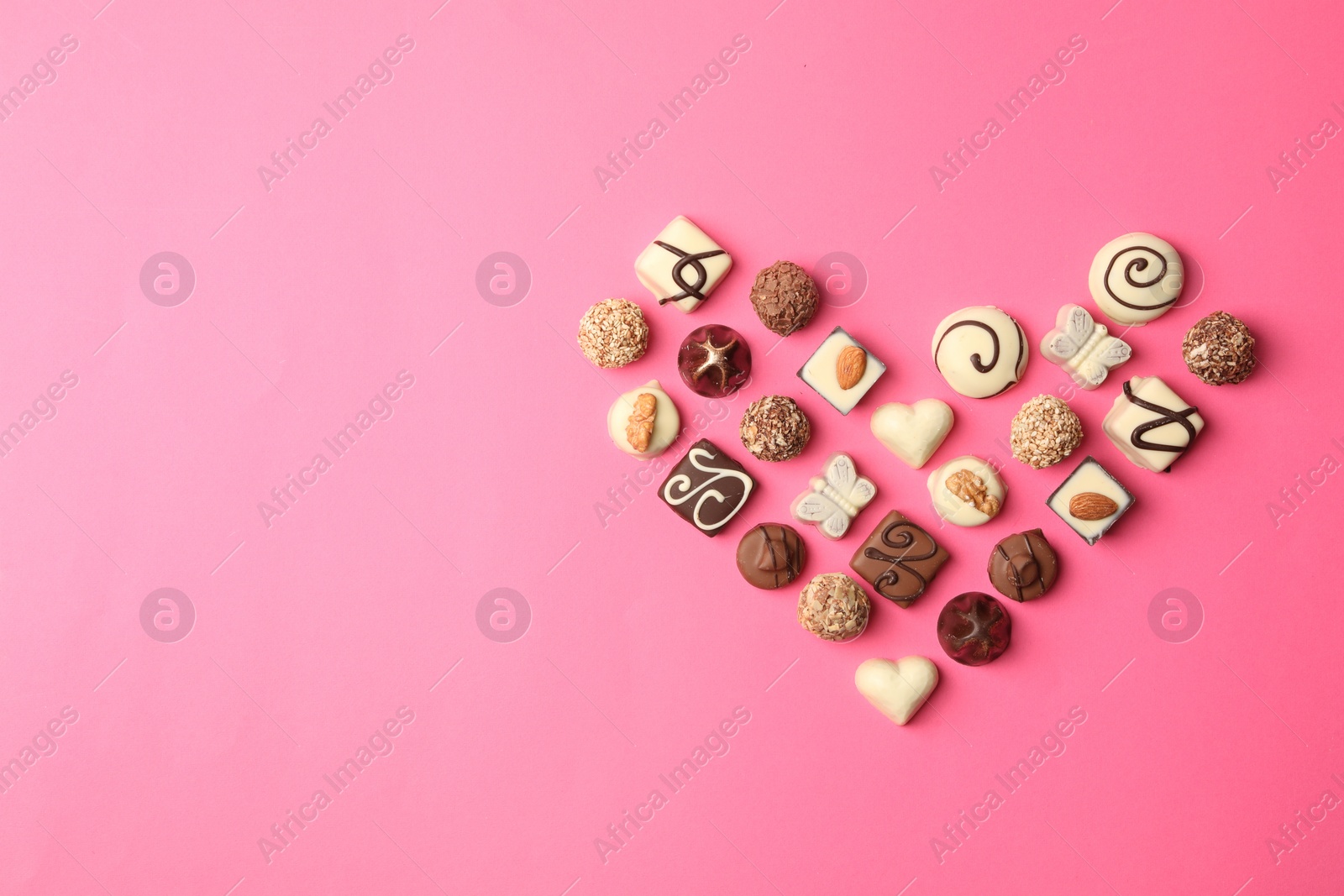 Photo of Heart made with delicious chocolate candies on pink background, top view. Space for text