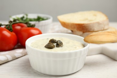 Photo of Creamy caper sauce in bowl on white wooden table, closeup