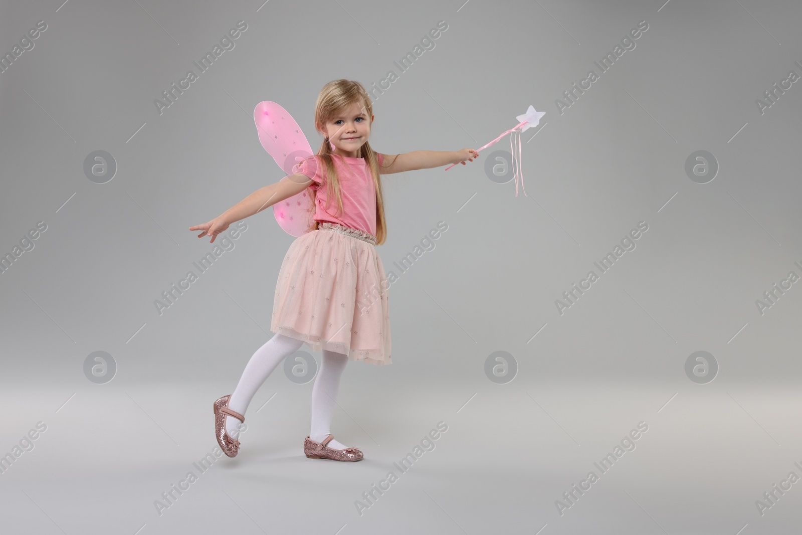 Photo of Cute little girl in fairy costume with pink wings and magic wand on light grey background