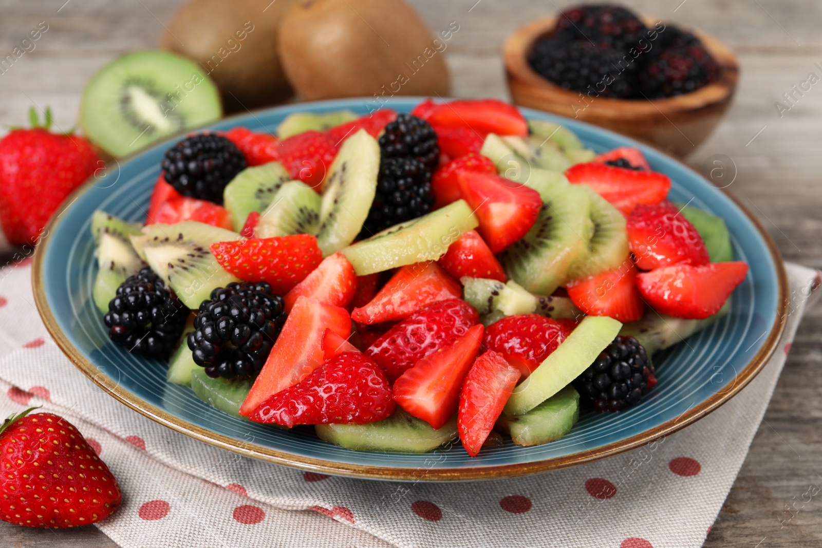 Photo of Plate of delicious fresh fruit salad on wooden table, closeup