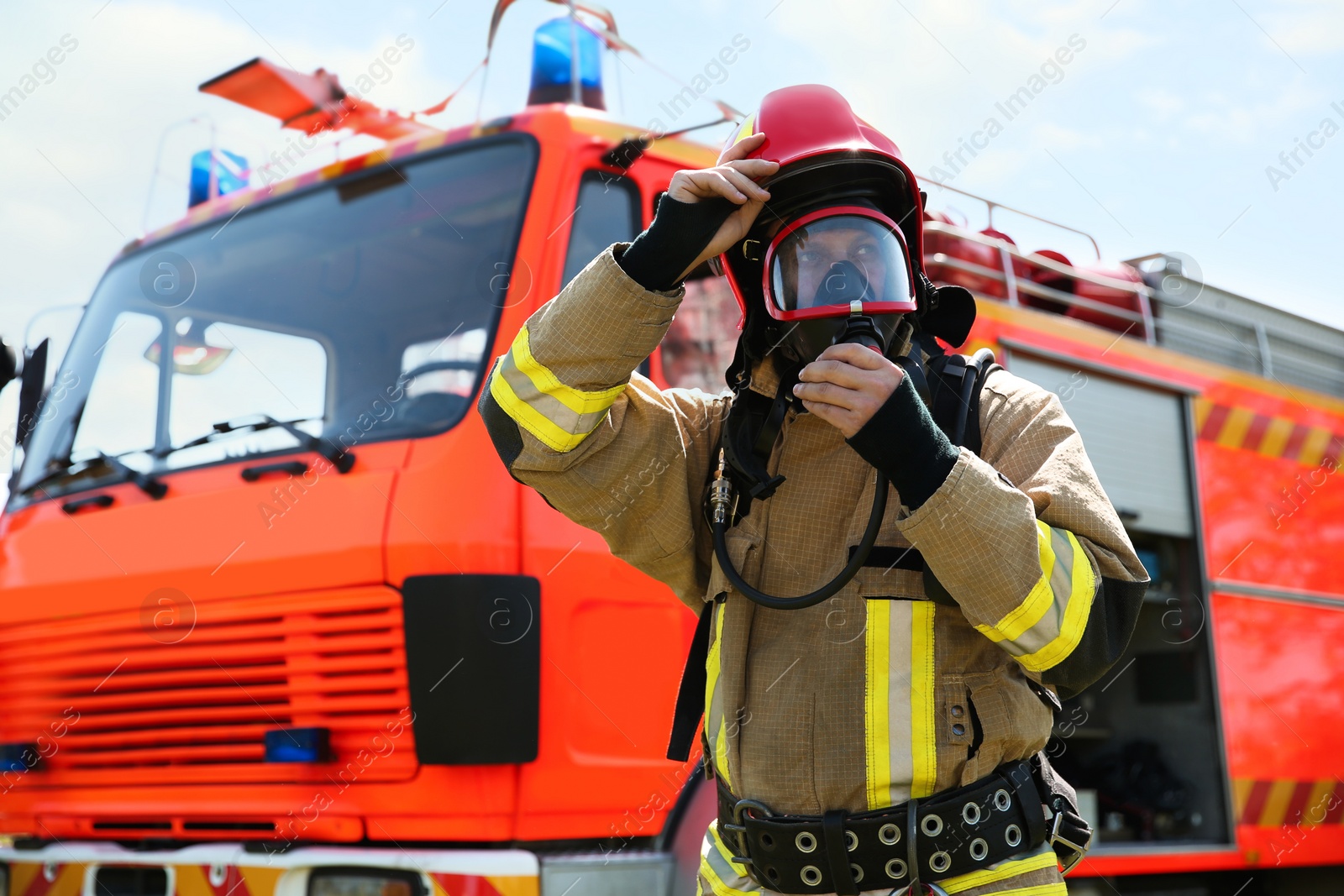 Photo of Firefighter in uniform wearing helmet and mask near fire truck outdoors