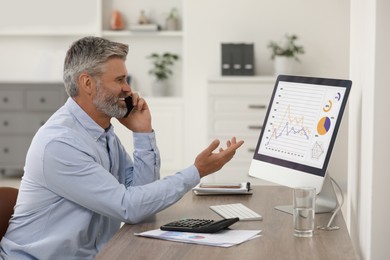 Professional accountant talking on phone and working at wooden desk in office