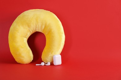 Photo of Yellow travel pillow and earphones on red background, space for text