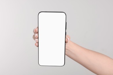 Woman holding smartphone with blank screen on light grey background, closeup. Space for text