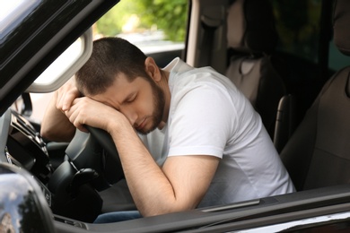 Tired man sleeping on steering wheel in his car