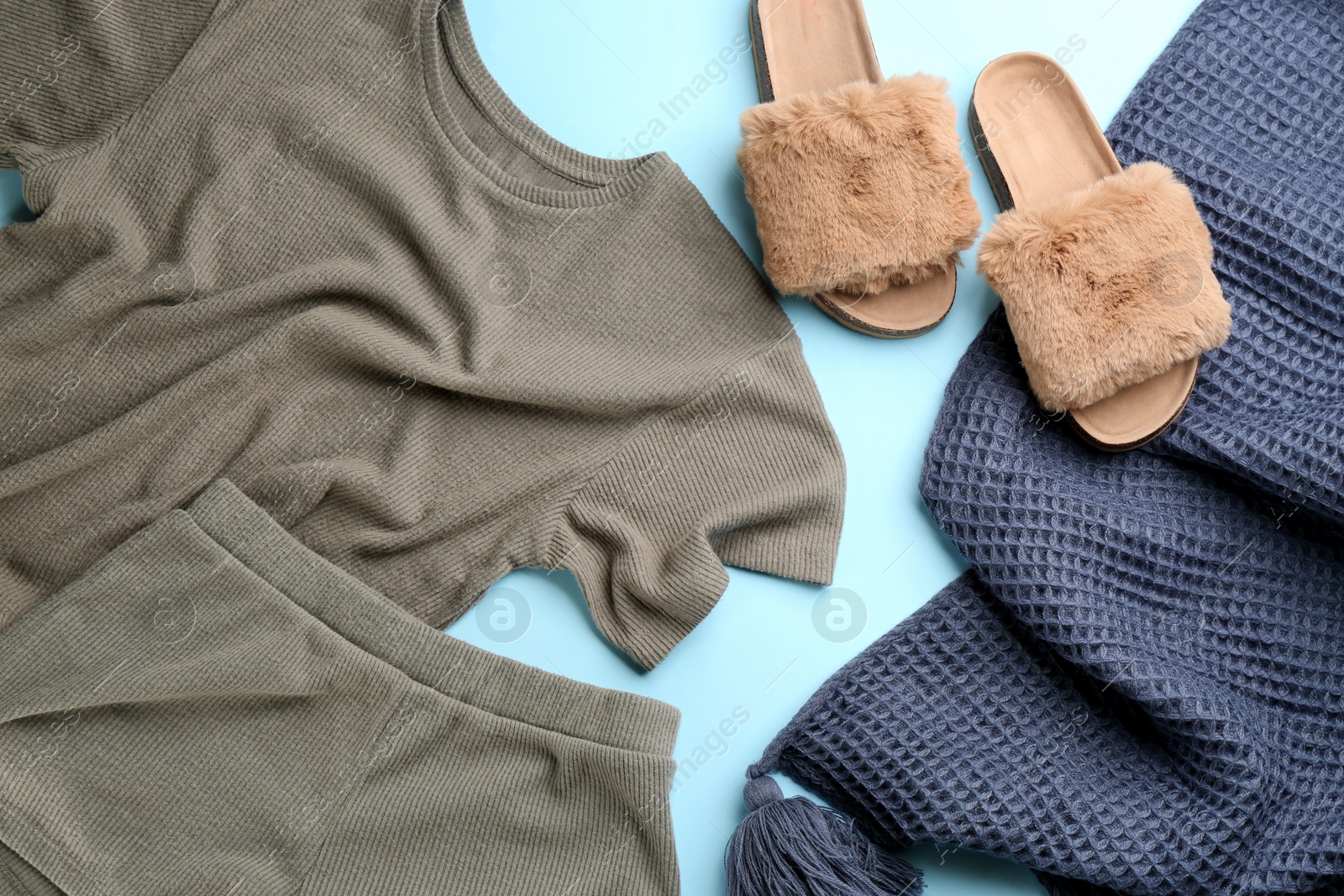 Photo of Pair of fluffy slippers, pajamas and blanket on light blue background, flat lay. Comfortable home outfit