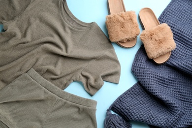 Photo of Pair of fluffy slippers, pajamas and blanket on light blue background, flat lay. Comfortable home outfit